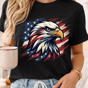 Może przedstawiać: Czarny t-shirt z szczeg&oacute;łową grafiką amerykańskiego bielika w patriotycznych barwach. Głowa orła jest biała, z czerwonymi i niebieskimi akcentami, na tle stylizowanej amerykańskiej flagi. Koszulka jest noszona przez osobę.