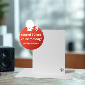 Könnte beinhalten: Eine weiße Grußkarte mit einem Mikrofon-Symbol und einem roten Kreis mit dem Text "record 30 sec voice message". Die Karte liegt auf einer weißen Oberfläche, im Hintergrund ist ein kleiner schwarzer Lautsprecher zu sehen.