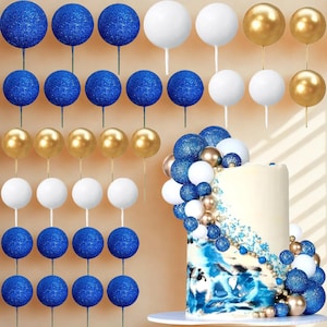 May include: An assortment of cake toppers in blue glitter, white, and gold. The toppers include spherical shapes on sticks, arranged in rows and decorating a cake with blue and white frosting.