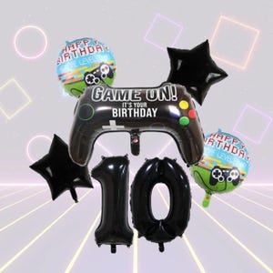 Könnte beinhalten: Eine Sammlung schwarzer und farbiger Luftballons für eine zehnte Geburtstagsfeier. Das Set enthält einen großen schwarzen Controller-Luftballon mit dem Text "GAME ON! IT'S YOUR BIRTHDAY", sternförmige Luftballons, runde Luftballons mit Controller-Grafik und schwarze Zahlenballons.