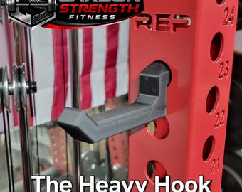 May include: A red weightlifting power rack with a black hook. The rack has the text "REP" and numbers 20-24. The text "The Heavy Hook" is at the bottom. The Carbon Strength Fitness logo is in the upper left.