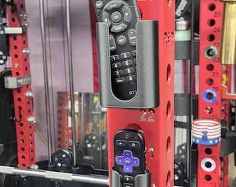 May include: Two black remote controls in gray holders attached to a red metal frame. The remotes have multiple buttons and are labeled with text. The frame has the number 25 and 22 printed on it.