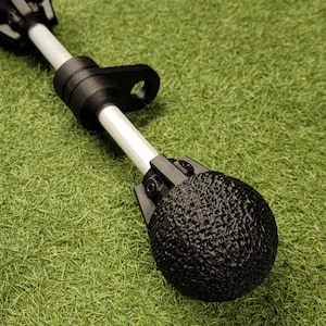 May include: A black and white object with a textured, spherical end. The object has a white pole and is set against a green, grassy background. The object appears to be a tool or a part of a larger device.