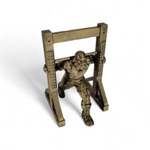 Op de afbeelding: Een bronskleurig beeldje van een gespierd figuur in een hemd en korte broek die een squat-oefening uitvoert. Het figuur is geplaatst in een structureel rekframe met verticale steunen met klinknagelachtige details.