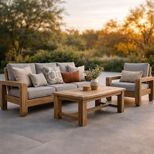 May include: Outdoor furniture set featuring a wooden sofa, armchair, and coffee table. The sofa and armchair have gray cushions and decorative pillows in various patterns and colors. A vase with greenery and a small tray are on the coffee table.