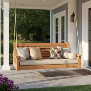 May include: A wooden porch swing suspended by thick ropes, featuring a slatted backrest and a long seat cushion. It includes two light gray square pillows, one solid beige square pillow, one patterned dark brown pillow, and two beige bolster pillows.