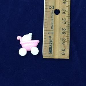 May include: A small, pink baby carriage with white wheels and a white canopy. The carriage is next to a wooden ruler with inch measurements, indicating its small size. The carriage is likely a decorative item or a cake decoration.