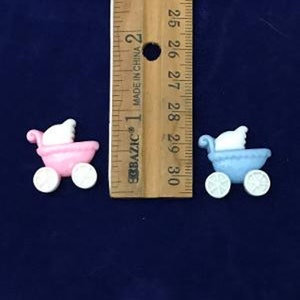 May include: Two miniature baby carriage decorations. One is pink, the other is blue. Each has white wheels and a white canopy. A wooden ruler with inch markings is in the background.