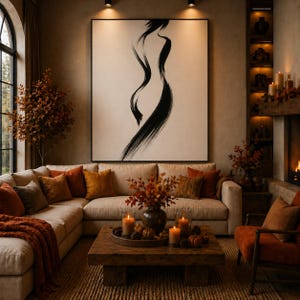 Puede incluir: Un salón acogedor con una gran obra de arte abstracta. Un sofá seccional beige está adornado con cojines naranjas y marrones y una manta a juego. Una mesa de centro de madera exhibe velas y calabazas, creando un ambiente cálido.