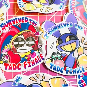 May include: Die-cut vinyl stickers featuring cartoon characters with colorful jester and rabbit designs. Each sticker displays the text I SURVIVED THE TADC FINALE in bold, multi-colored lettering. The artwork uses vibrant shades of red, blue, and yellow.