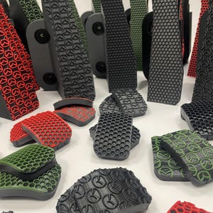 Op de afbeelding: Een assortiment van zwarte, rode en groene rubberen pads en strips met textuur. De pads hebben verschillende patronen, waaronder honingraat- en cirkelvormige ontwerpen. Sommige strips zijn lang en rechthoekig, andere kleiner en gebogen.