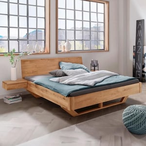 May include: A light oak bed frame with a headboard and a floating bedside table. The bed is made with blue and grey bedding and pillows. The room has large windows with a mountain view and decorative vases.