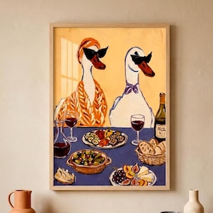 May include: A framed art print depicts two geese wearing sunglasses, seated at a table laden with food and wine. The table is set with plates of olives, cheese, fruit, and bread. A bottle of wine and glasses of red wine are also present.