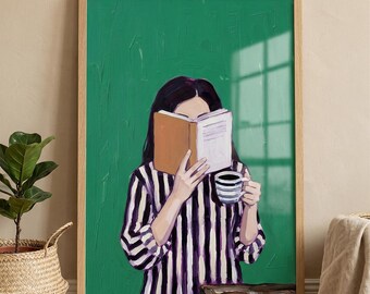 May include: A framed art print depicts a person reading a book, holding a striped mug. The person wears a striped shirt with purple and white stripes. The background is a solid green color. A potted plant in a woven basket is in the foreground.