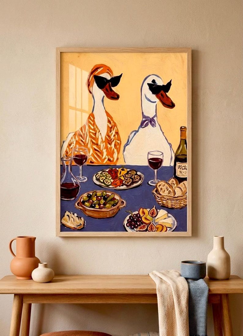 May include: A framed art print depicts two geese wearing sunglasses, seated at a table laden with food and wine. The table is set with plates of olives, cheese, fruit, and bread. A bottle of wine and glasses of red wine are also present.