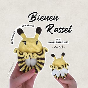 May include: A crocheted bee-shaped rattle in yellow and brown, with the text "Bienen Rassel" and "PDF HÄKELANLEITUNG - deutsch-". The rattle has a rounded body with striped detailing and small antennae.
