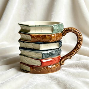 May include: A ceramic mug designed to look like a stack of books. The mug is in shades of brown, green, red, and blue, with a decorative handle. The mug's design mimics a stack of books, each with a different colour and a detailed spine.