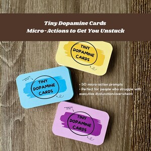 May include: Three colourful card decks labelled "Tiny Dopamine Cards" with the tagline "Micro-Actions to Get You Unstuck." The cards are in yellow, blue, and purple, with rounded corners. The text "50 micro-action prompts" is also visible.