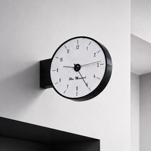 May include: A double-sided wall clock with a black circular frame and a white face. The clock features black numerals from 1 to 12, black hands, and the text The Marshal printed in a script font on the center of the white clock face.