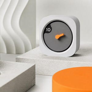 Pode incluir: Um temporizador quadrado branco com cantos arredondados e um mostrador circular cinzento-escuro. O mostrador apresenta o número 10 em branco e inclui um único ponteiro laranja brilhante apontado para o lado superior direito do mostrador.