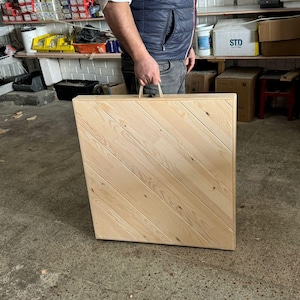 May include: A light-colored wooden table with a diagonal plank design is being carried by a person. The table has a handle made of rope. The table is rectangular and appears to be new.