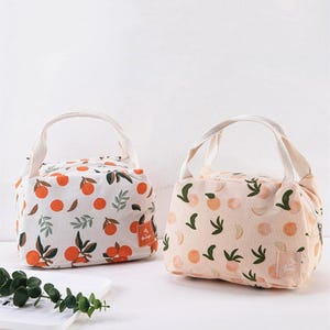 May include: Two rectangular lunch bags with top handles and zip closures. The left bag is white with an orange fruit and green leaf pattern. The right bag is light peach with a peach fruit and green leaf pattern, featuring a small label reading Peach.