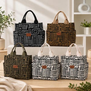 Puede incluir: Cinco bolsos tote rectangulares con dos asas y un bolsillo exterior, cada uno con un patrón de líneas geométricas. Los bolsos están disponibles en combinaciones de colores negro y gris, marrón y negro, verde oliva y negro, blanco y negro, y negro y blanco.