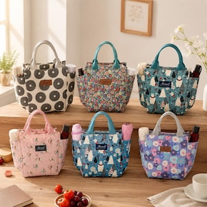 May include: Six insulated lunch bags with handles and side pockets are displayed. The bags feature various patterns, including floral, bear and tree, and polka dot designs. Each bag has a small label that reads "Mancal".