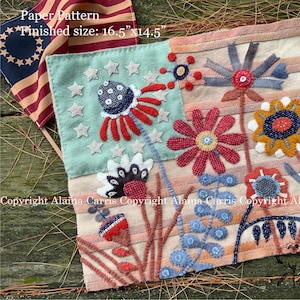 May include: A fabric craft pattern featuring a stylized American flag background with appliqued floral designs in red, blue, and yellow. The rectangular piece measures 16.5 inches by 14.5 inches and includes embroidered stars and various flower shapes.