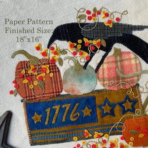 May include: A paper pattern for a textile craft featuring a black crow, pumpkins in plaid and solid colors, and a rectangular blue and gold sign with the text 1776 and stars. The finished size is listed as 18 inches by 16 inches on the pattern.