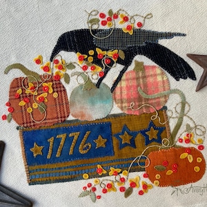 May include: A textile applique featuring a black crow, four pumpkins in various plaid and solid fabrics, and a rectangular blue and gold banner with the text 1776 and star motifs. The design is embellished with small red and yellow felt flowers.