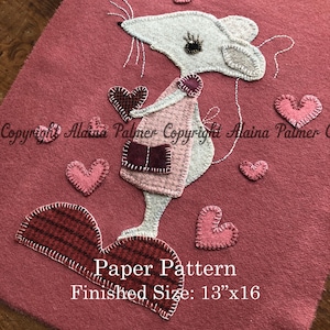 May include: A felt applique pattern featuring a white mouse holding a red heart. The mouse is surrounded by pink hearts and the text "Paper Pattern Finished Size: 13"x16"