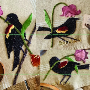 Puede incluir: Tres tapices de pared de fieltro bordados con pájaros negros con detalles rojos y amarillos posados ​​en tallos verdes con flores rosas y rojas. El fondo es una tela de lino natural.