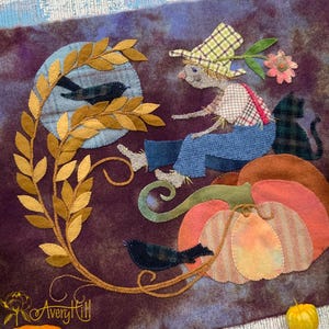 May include: A fabric wall hanging featuring a scarecrow in a plaid hat and blue overalls sitting on a large orange pumpkin. The scene includes a black cat, two black birds, a golden leaf vine, and a purple mottled background. The text Avery Hill is visible.