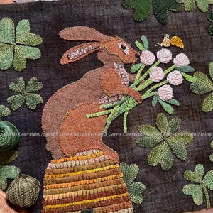 May include: A brown rabbit with long ears sits on a beehive, surrounded by green four-leaf clovers and pink flowers. The rabbit is looking at a butterfly.