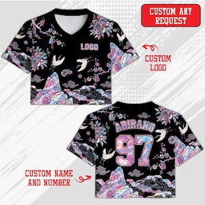 Puede incluir: Top corto negro con diseño de cuello en V, con un estampado floral y de paisaje montañoso en colores pastel. La camisa tiene la palabra "LOGO" impresa en la parte delantera. La parte trasera de la camisa tiene la palabra "ARIRANG" y el número "97".