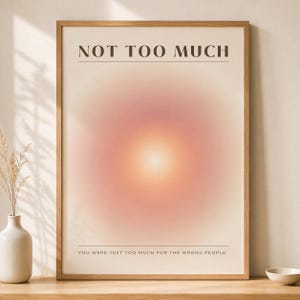 Könnte beinhalten: Ein gerahmter Kunstdruck mit dem Text „NOT TOO MUCH“ oben und „YOU WERE JUST TOO MUCH FOR THE WRONG PEOPLE“ unten. Das Kunstwerk zeigt einen weichen, kreisförmigen Farbverlauf aus Rosa- und Orangetönen, der eine warme, einladende Ästhetik erzeugt.