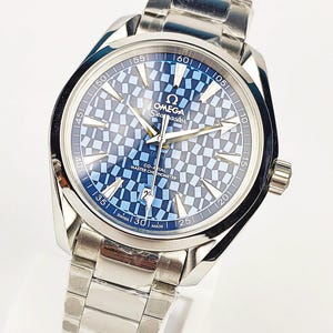 Op de afbeelding: Een zilverkleurig roestvrijstalen Omega Seamaster horloge met een blauwe en lichtblauwe wijzerplaat met ruitpatroon. Het horloge heeft zilveren wijzers, uurmarkeringen, een datumvenster op de zes uur positie en de tekst OMEGA Seamaster Co-Axial Master Chronometer.