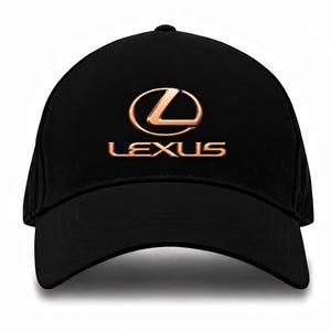 Puede incluir: Una gorra de béisbol negra que presenta el logotipo de Lexus y la palabra LEXUS bordada en un color cobre metálico en la parte frontal central. La gorra tiene una corona estructurada, una visera curva y una construcción de tela negra.