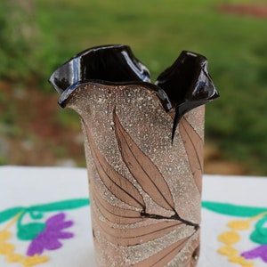 Peut inclure: Un vase en céramique brun avec un bord noir et un motif de feuilles. Le vase a une surface texturée et une forme unique.