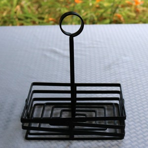 May include: Black metal condiment holder with a circular handle. The holder has multiple tiers for holding bottles or jars.