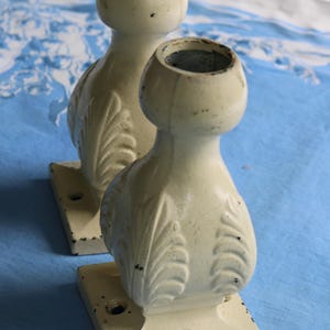 Peut inclure: Deux pieds de meubles décoratifs en fonte de couleur blanc cassé avec un motif de feuilles. Les pieds ont une base carrée avec un trou au centre.
