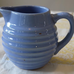 Puede incluir: Jarra de cerámica azul claro con asa y boquilla. La jarra tiene un diseño acanalado alrededor del cuerpo. La jarra mide aproximadamente 15 cm de alto y 13 cm de ancho.