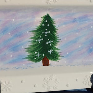 May include: A white ceramic rectangular serving dish with a painted design of a green Christmas tree with white snowflakes on a light blue and purple background.