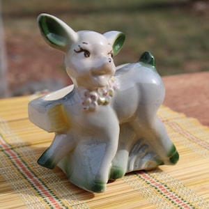 May include: A ceramic planter shaped like a deer with green ears and a floral design around its neck. The planter is light blue and white with green accents.