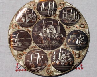 May include: A round copper plate with an intricate design featuring various scenes of Istanbul, Turkey. The plate is decorated with a floral pattern and features images of the Hagia Sophia, the Galata Tower, and the Bosphorus Bridge.