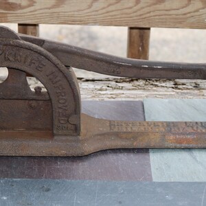 May include: A vintage cast iron cigar cutter with a lever handle. The cutter is labeled "The Champion Knife Improved".