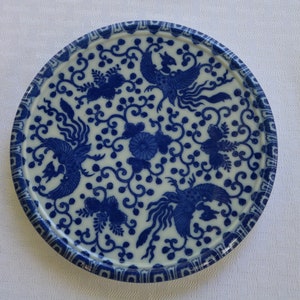 Op de afbeelding: Een wit keramiek bord met een blauw en wit ontwerp van gestileerde vogels en bloemmotieven.