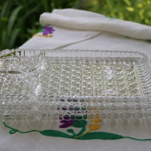 Puede incluir: Una bandeja de servir de vidrio transparente con una sección dividida. La bandeja tiene un patrón de diamante y está hecha de vidrio grueso.