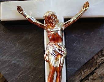 May include: A white wooden crucifix with a silver-colored Jesus figure. The figure has a red-brown body and is wearing a silver-colored loincloth. The crucifix has a brown inscription that reads "INRI".